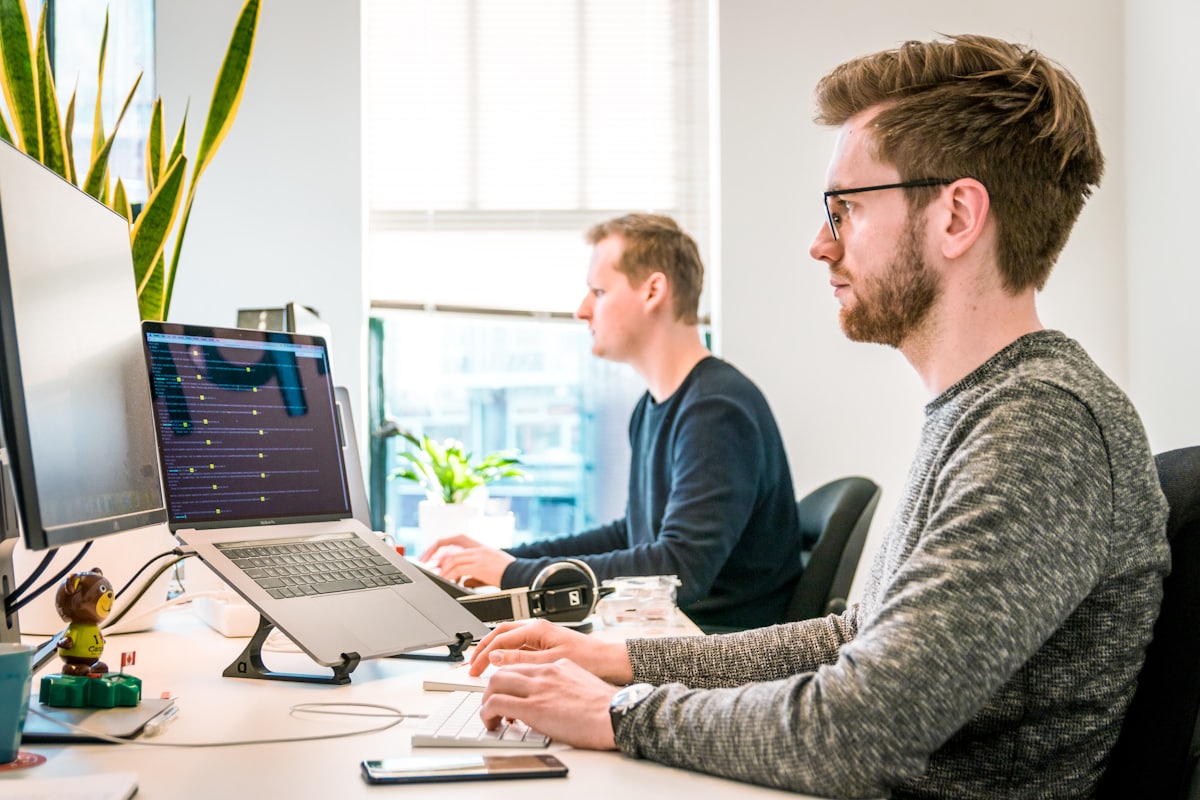 Two engineers working at adjacent desks, dashboards open on their screens